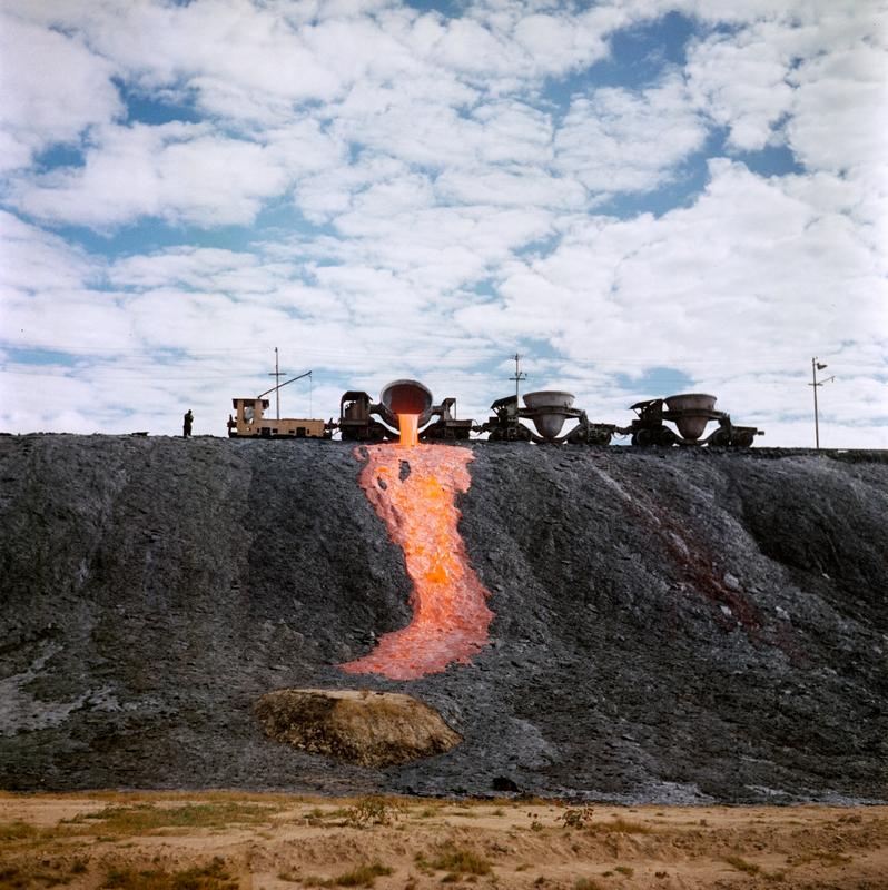 Color image of molten material being dumped down a hillside from a train